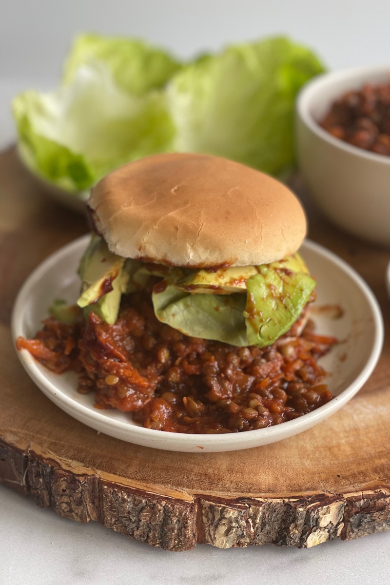close up of a vegan sloppy joe on a plate on a wood cutting board in front of a plate of lettuce leaves
