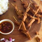 3 seitan skewers on a wood cutting board next to a bowl of rice and a bowl of teriyaki sauce