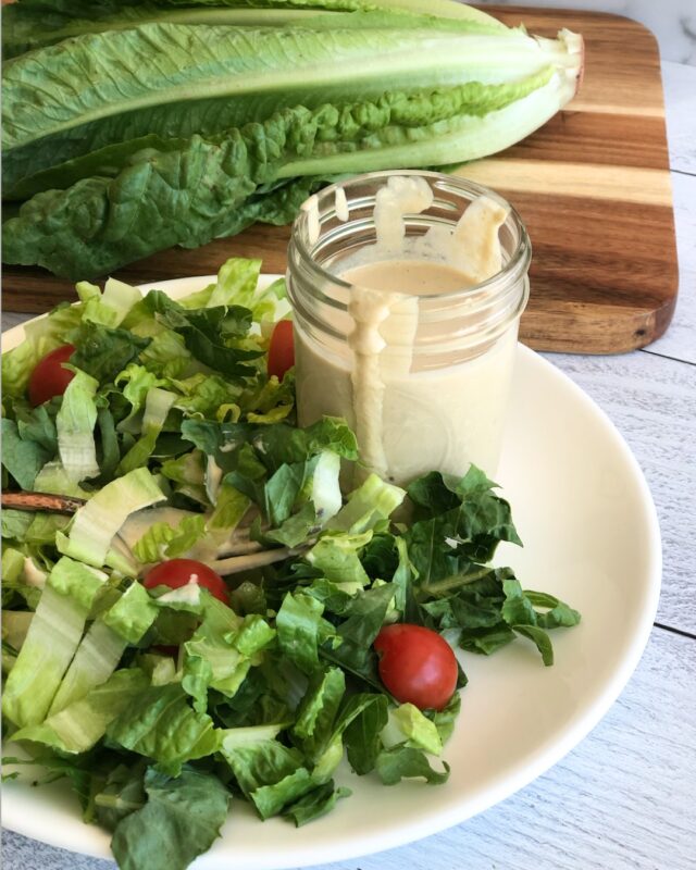 green salad on a plate with a jar of Caesar dressing, in front of a cutting board with a head of romaine lettuce on it