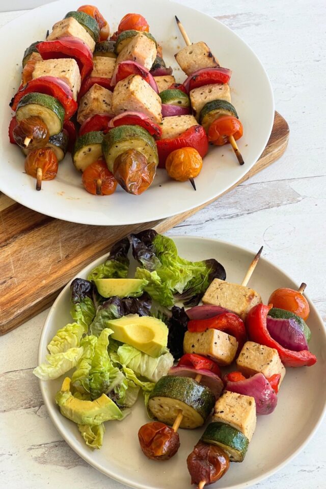 plate of kebabs on a wood cutting board above a plate of 2 kebabs and salad