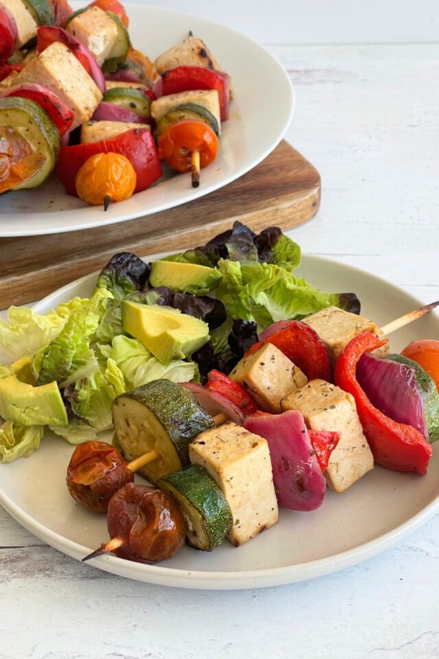 close up plate of kebabs and salad in front of a cutting board with a plate of kebabs on it