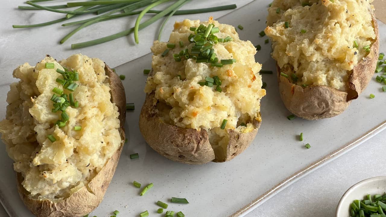 3 baked and stuffed potatoes on a white serving platter surrounded by herbs