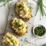 white platter with three stuffed potatoes and chives on top surrounded by chives