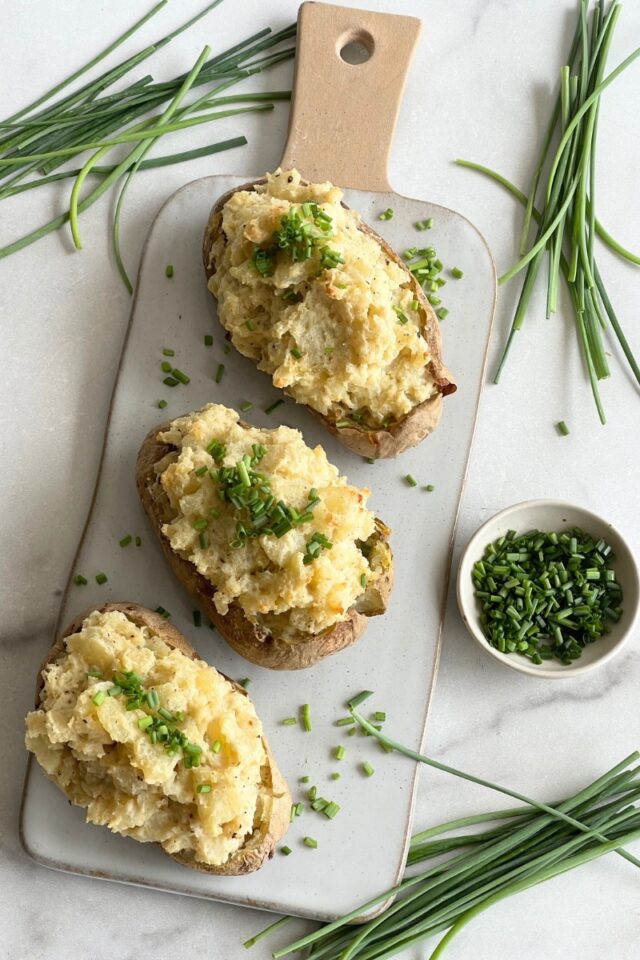 white platter with three stuffed potatoes and chives on top surrounded by chives