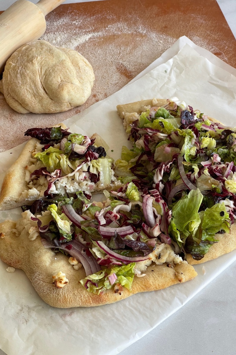 salad pizza on parchment paper in front of a ball of pizza dough and a rolling pin