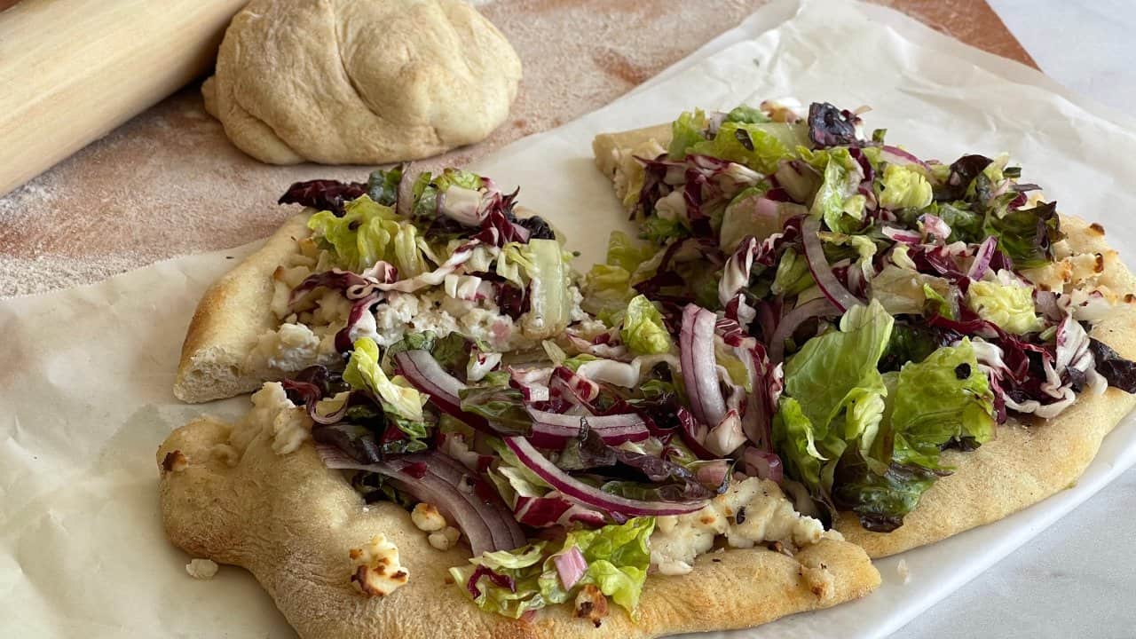 salad pizza on parchment paper in front of a rolling pin and ball of dough