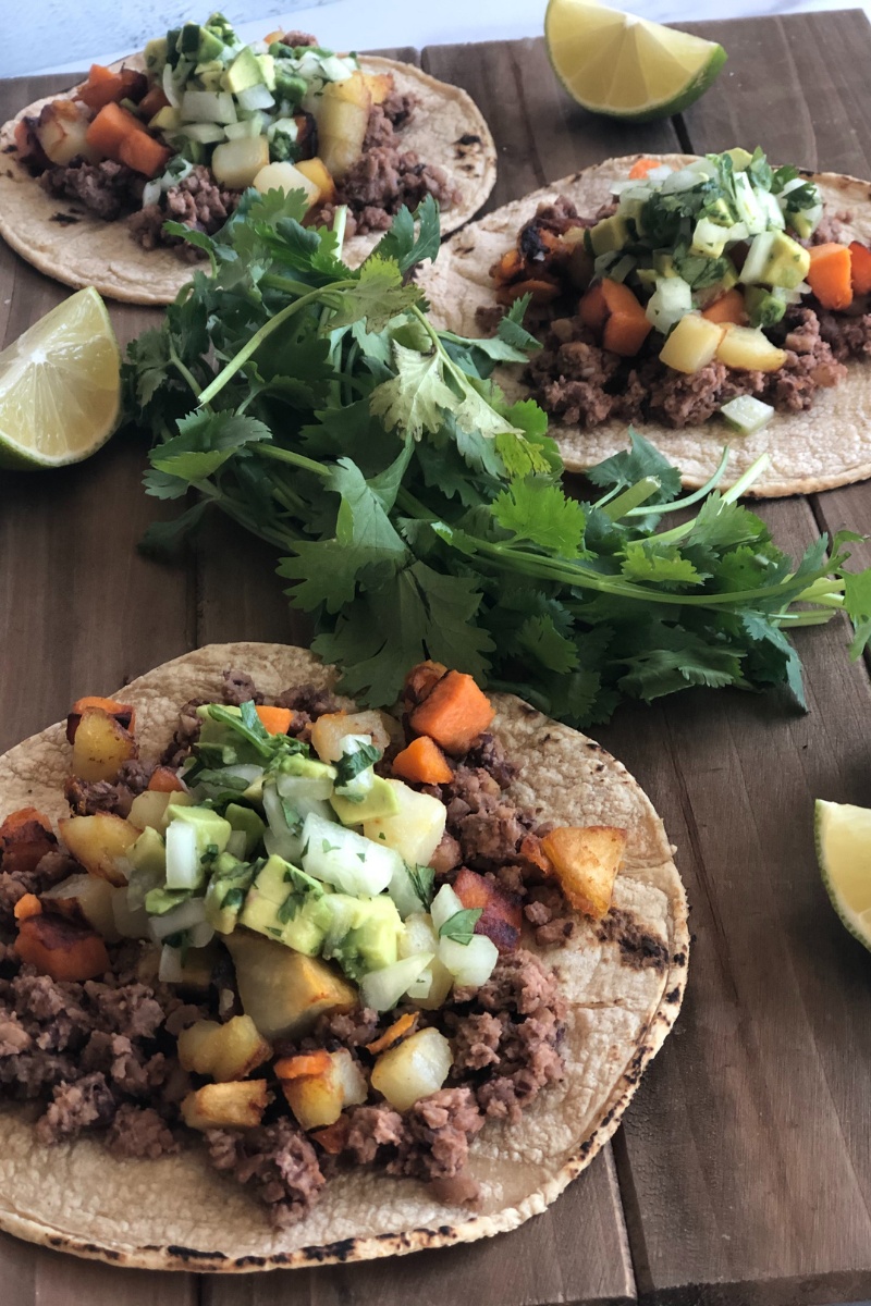 3 open face tacos on a wood board with cilantro and lime wedges