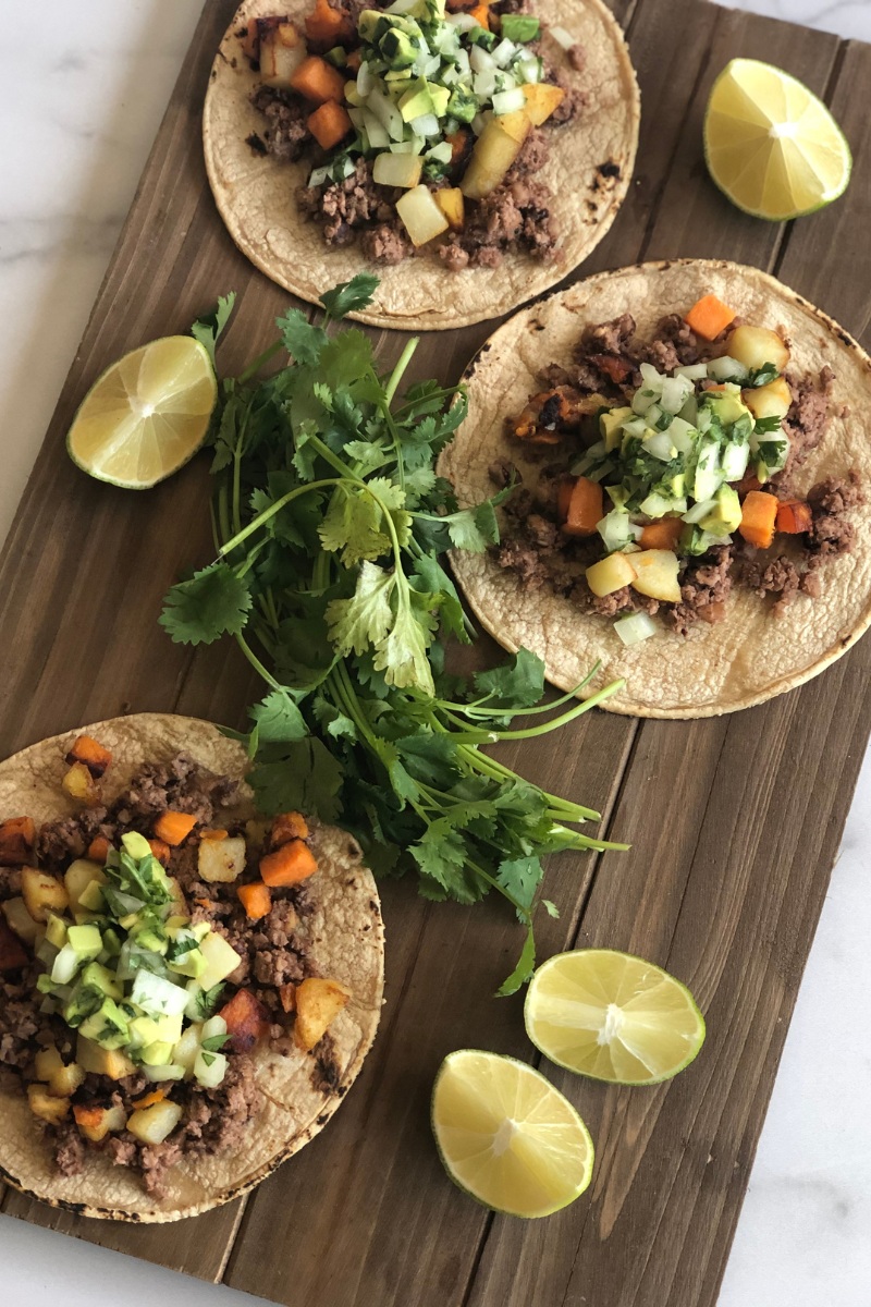 three open faced tacos on a wood board with lime wedges and cilantro