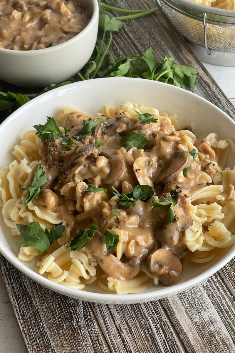 bowl of mushroom stroganoff on a wood board in front of a small bowl of noodles