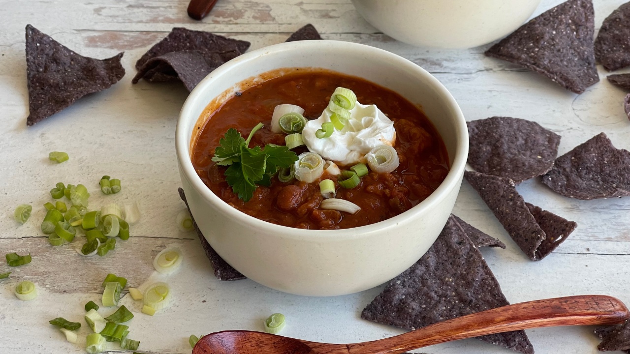 Bowl of chili topped with green onions and sour cream surrounded by blue tortilla chips
