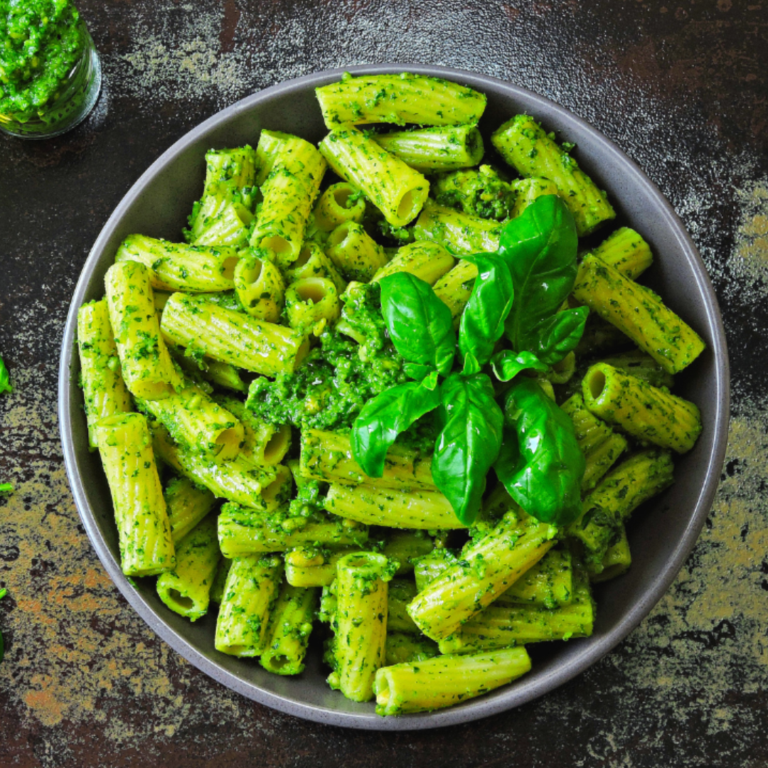 bowl of rigatoni pasta tossed wit pesto sauce and topped with basil leaves