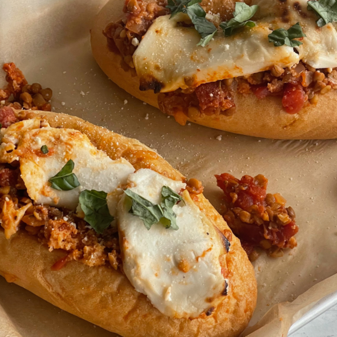 two sub rolls filled with bolognese sauce and topped with melted cheese on parchment paper