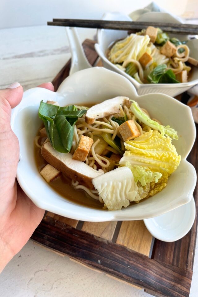 hand holding a bowl of ramen in front of another bowl of ramen