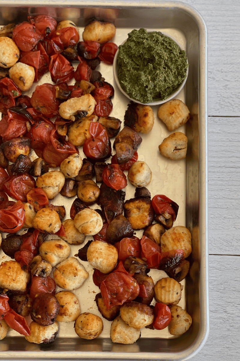 sheet pan with roasted gnocchi and tomatoes on it next to a bowl of pesto