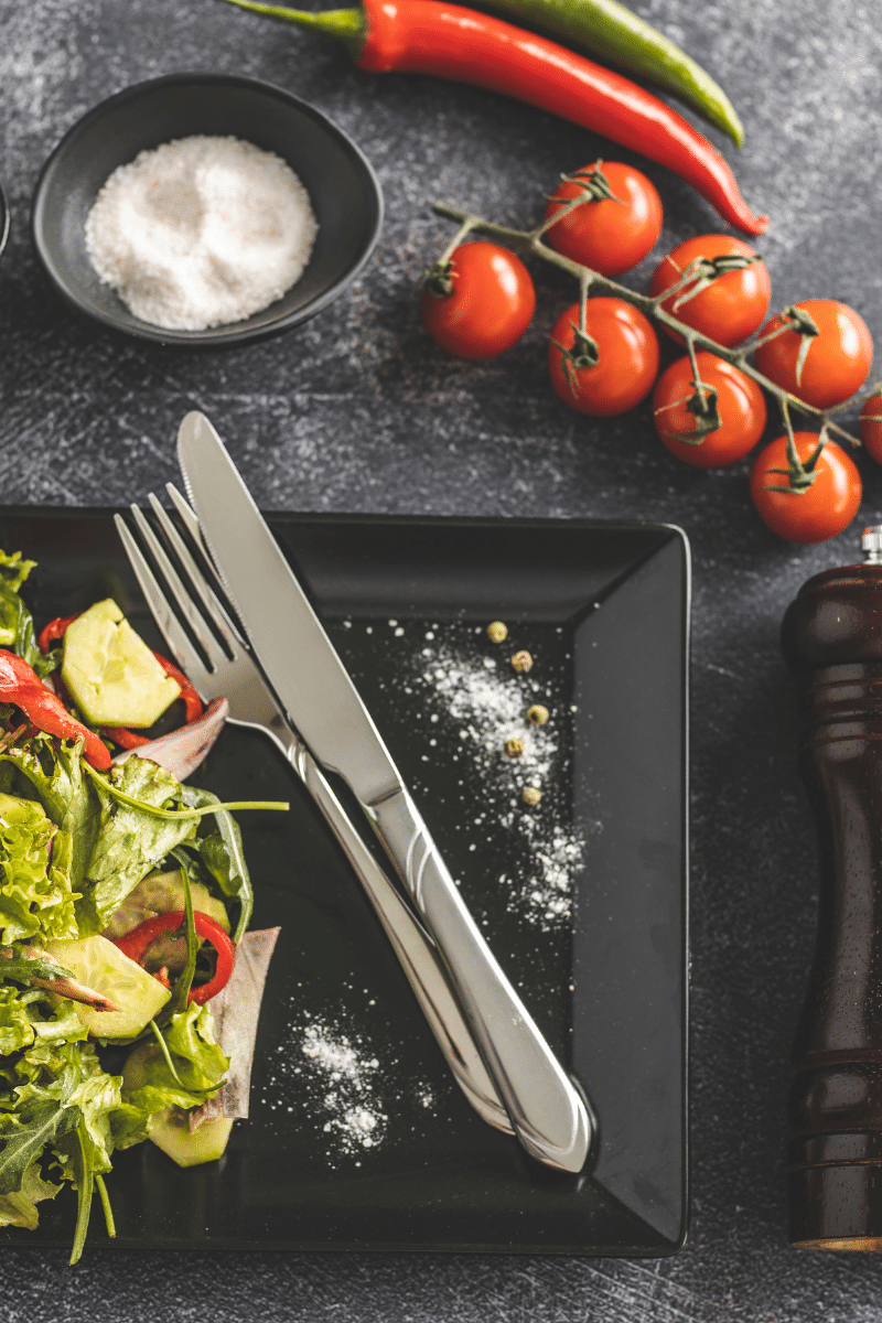 plate of salad with a fork and knife on it next to baby tomatoes on the vine