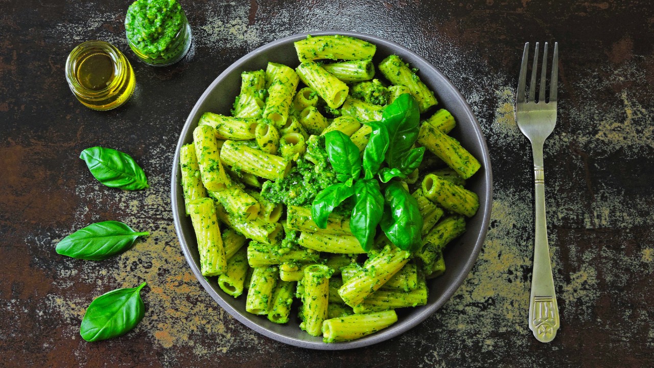 bowl of rigatoni pasta with pesto sauce on a wood table with a fork