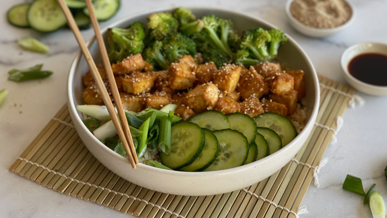 bowl of broccoli, tofu and cucumbers in a bowl with chopsticks on top of a sushi mat
