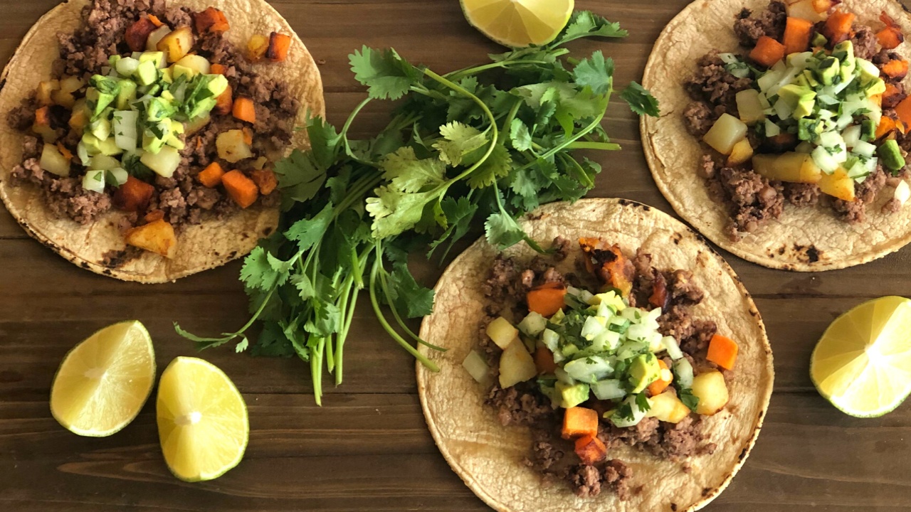 three open-faced tacos with beans, potatoes and guacamole on a wood table