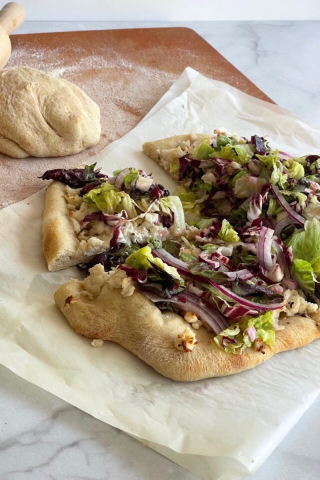 salad pizza on a piece of parchment paper on a marble counter next to a ball of dough