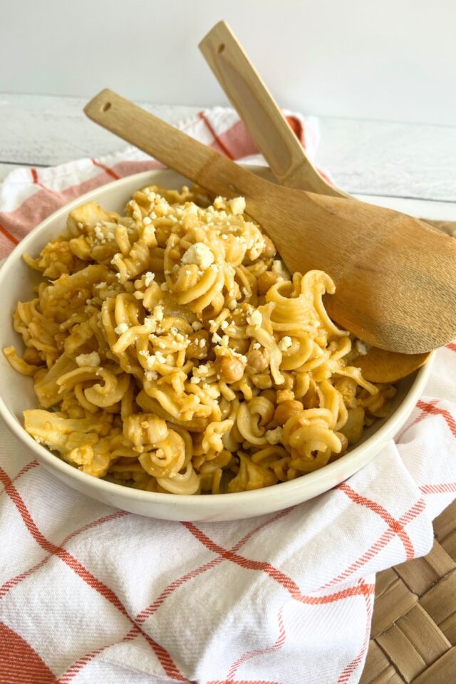 Bowl of pasta salad with wooden servers in it on top of an orange and white dish towel