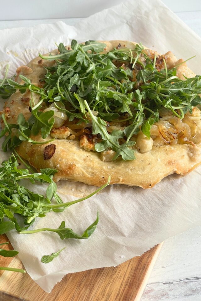 Pizza with arugula on parchment paper on top of a cutting board on a marble countertop