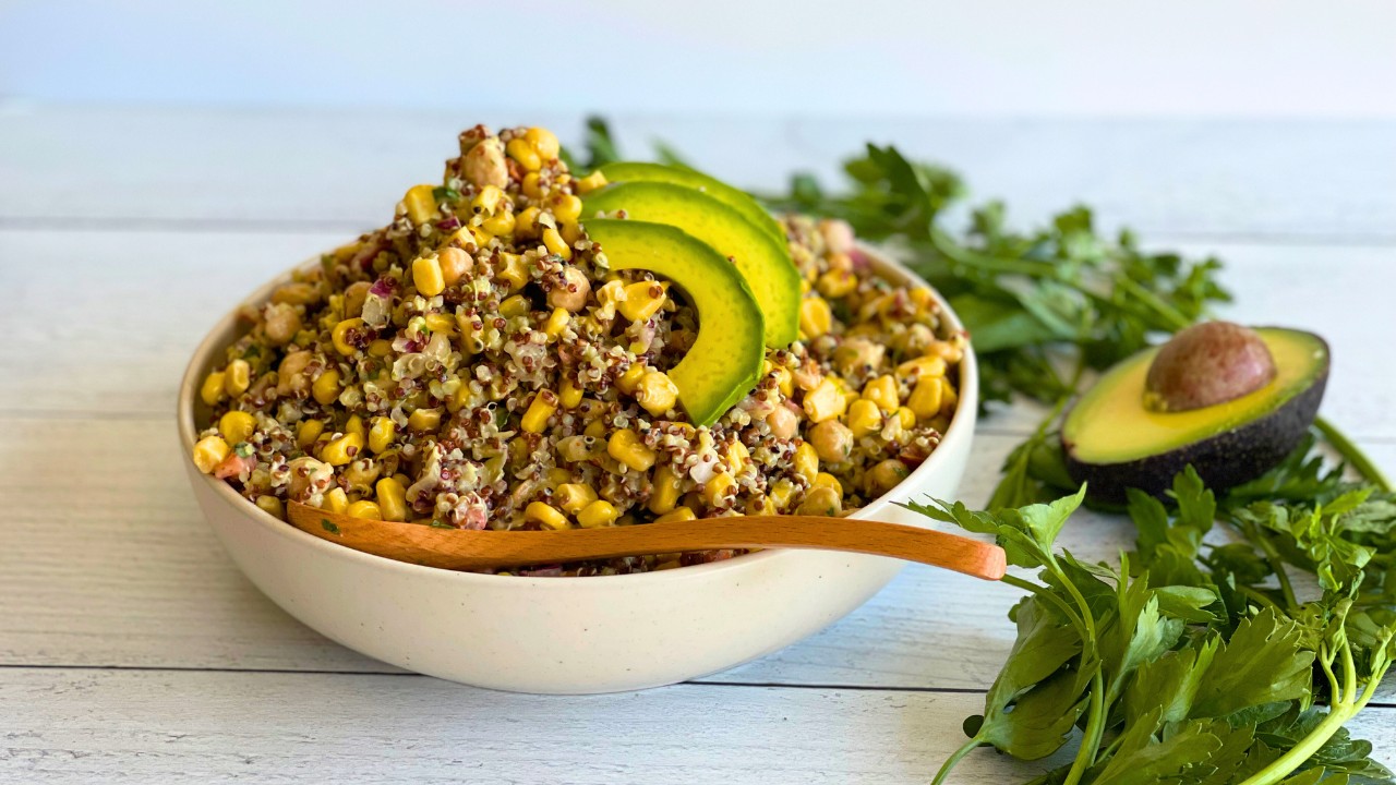 bowl of corn and quinoa salad on a counter next to cilantro and an avocado