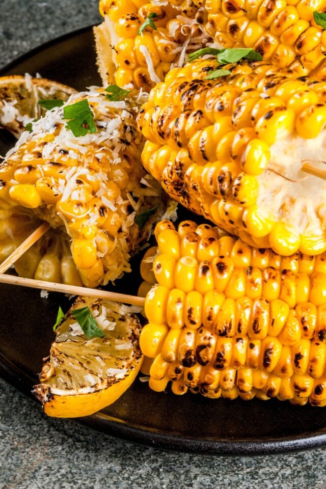 several grilled ears of corn cut in half on skewers on a plate