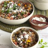 two bowls of lentil tabbouleh salad on a green placemat next to a bowl of feta cheese