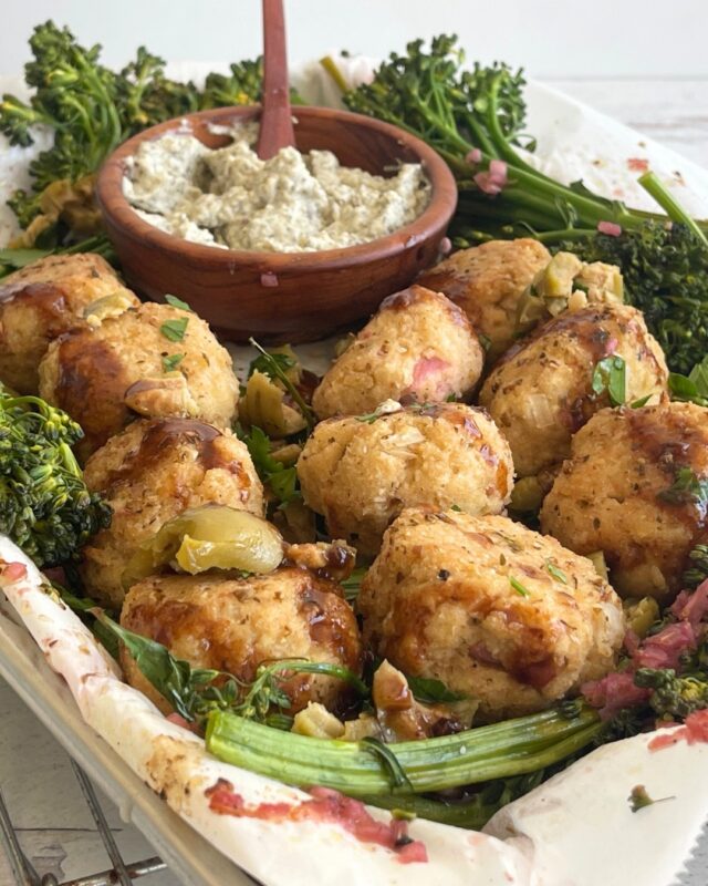 Sheet pan with tofu meatballs and broccolini and wooden bowl of garlic sauce with a wooden spoon in it