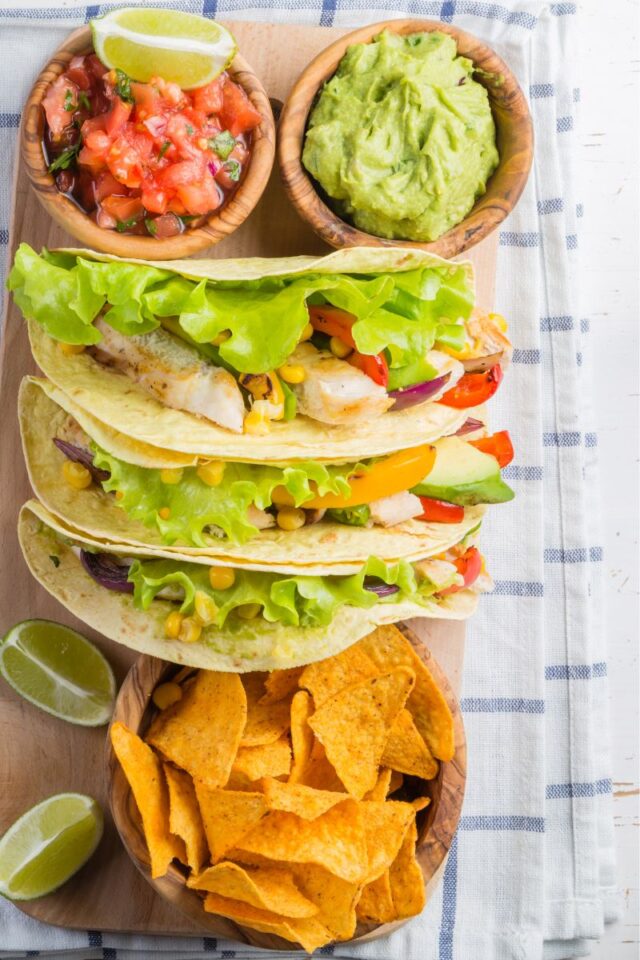 Board with tacos, tortilla chips, salsa and guacamole