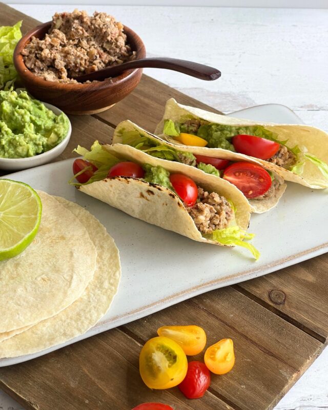 3 tacos on a cutting board next to bowls of guacamole and vegan chorizo