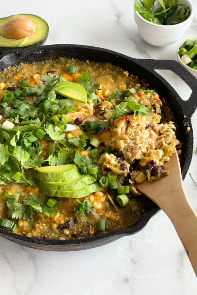 Skillet with an enchilada bake in it with a wooden spoon on the side