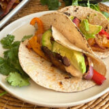 plate of tacos on a wicker placemat next to a sheet pan of vegetables