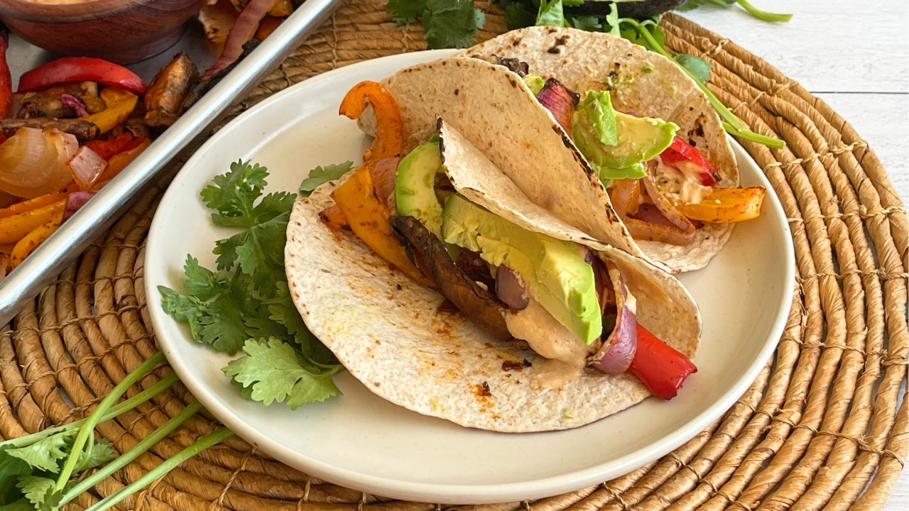 plate of tacos on a wicker placemat next to a sheet pan of vegetables