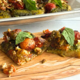 two slices of pizza on an oblong wood cutting board that's sitting in front of a sheet pan with more pizza