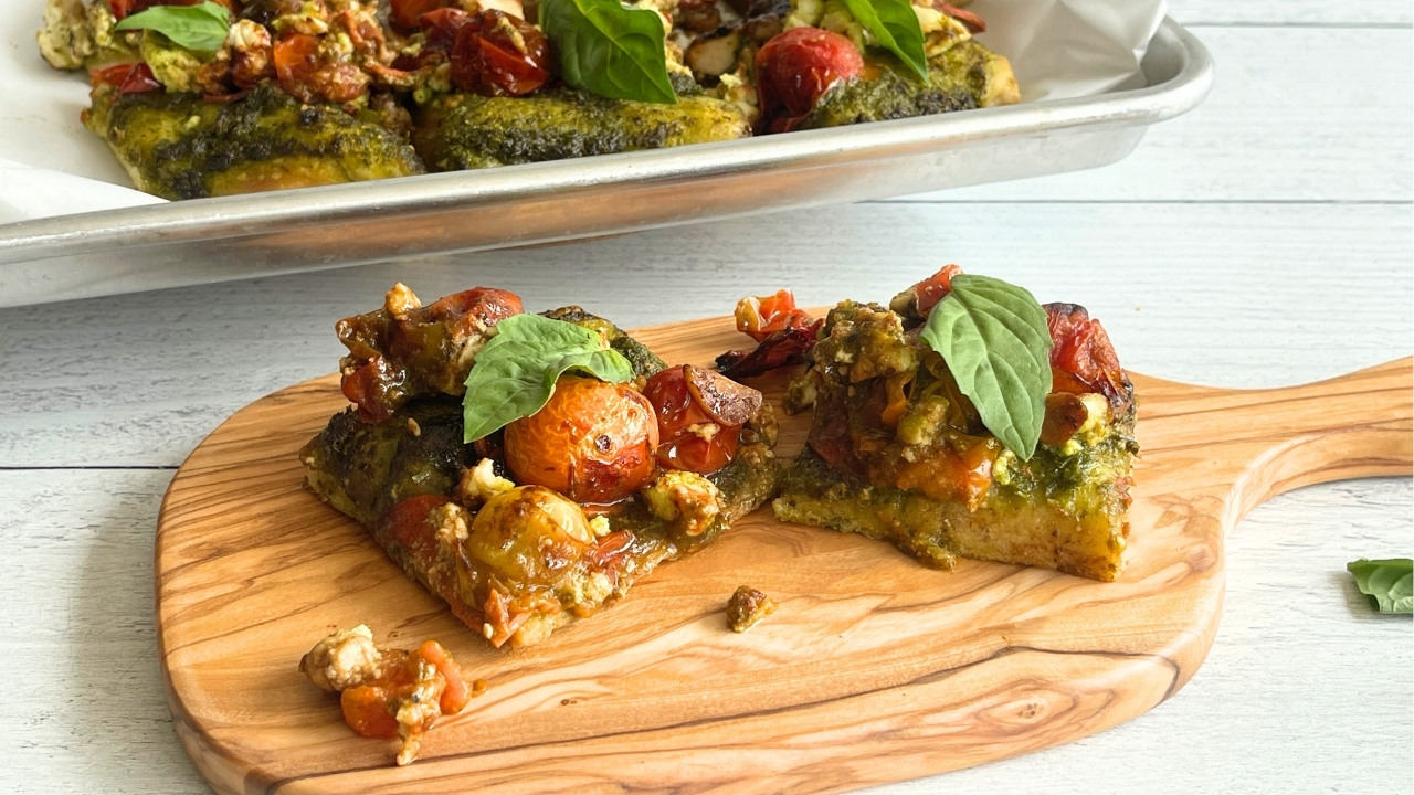 two slices of pizza on an oblong wood cutting board that's sitting in front of a sheet pan with more pizza