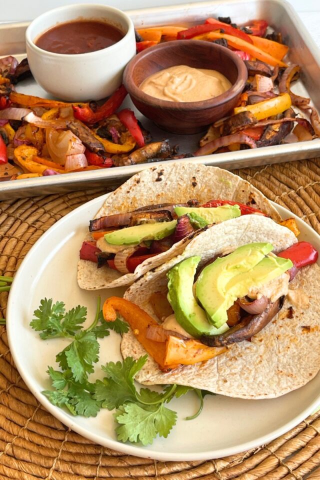 a plate of tacos in front of a sheet pan of vegetables