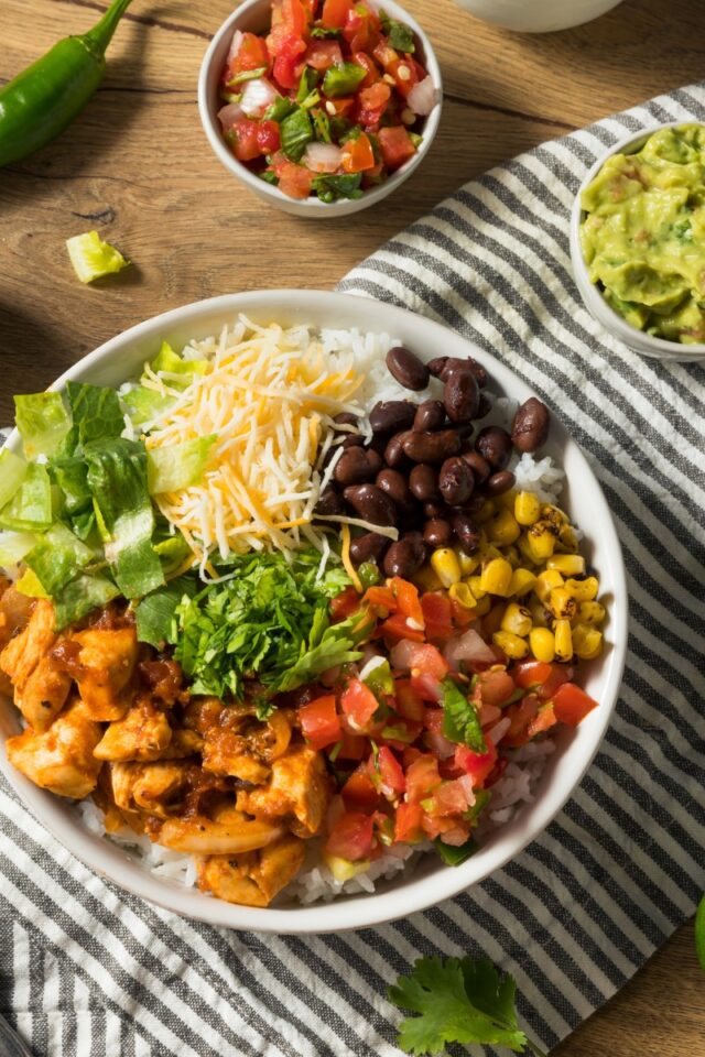 bowl full of beans, cheese, corn, lettuce. chicken and tomatoes on a wood table