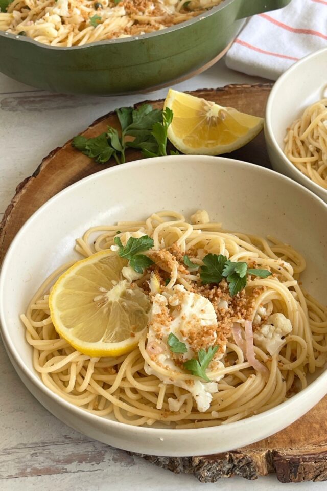 Bowl of pasta on a wood board next to a lemon wedge and sprigs of parsley