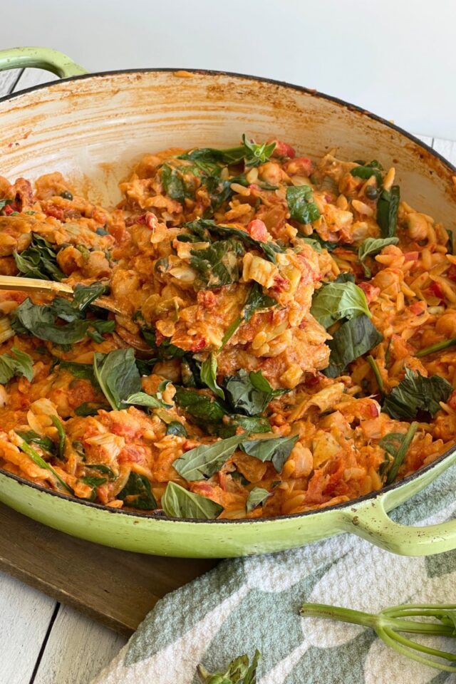 casserole dish with orzo and tomatoes, with a spoon holding a spoonful of the dish inside the pan