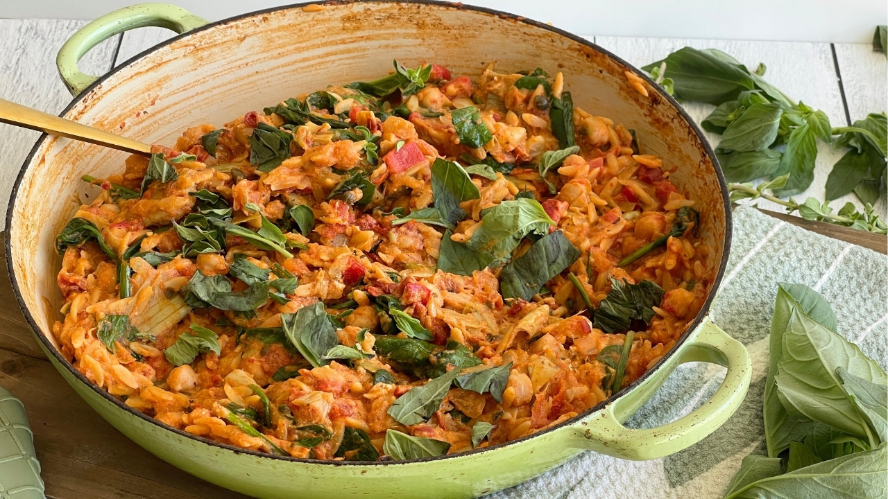 green round Dutch oven with orzo, tomatoes and vegetables on a countertop