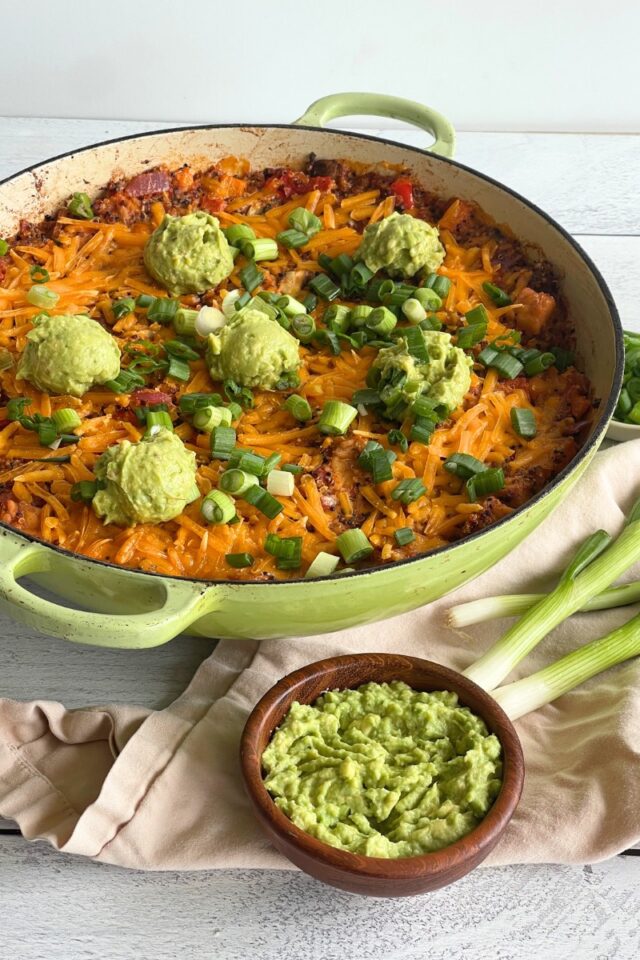 Green casserole dish with a Mexican rice dish next to a bowl of guacamole and two green onions