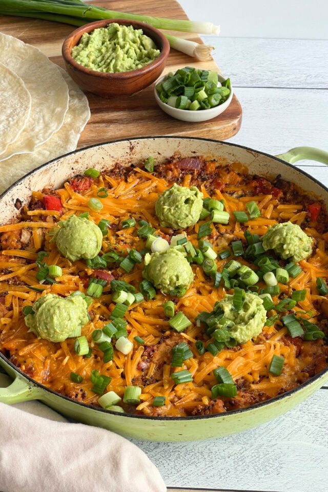 Casserole dish with a Mexican rice dish next to flour tortillas and bowls of guacamole and green onions