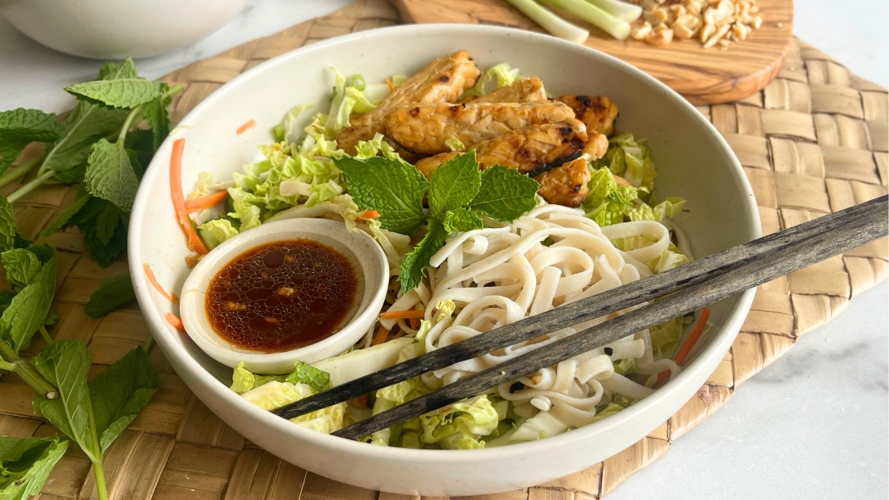 rice noodles, vegetables and tempeh in a bowl with chopsticks