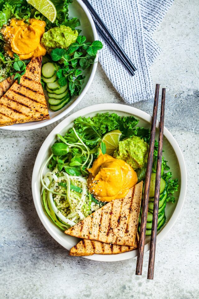 two bowls with chopsticks full of zoodles, greens, grilled tofu and hummus