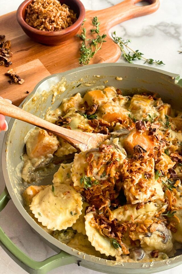 Green skillet full of ravioli with someone scooping some up on a spoon