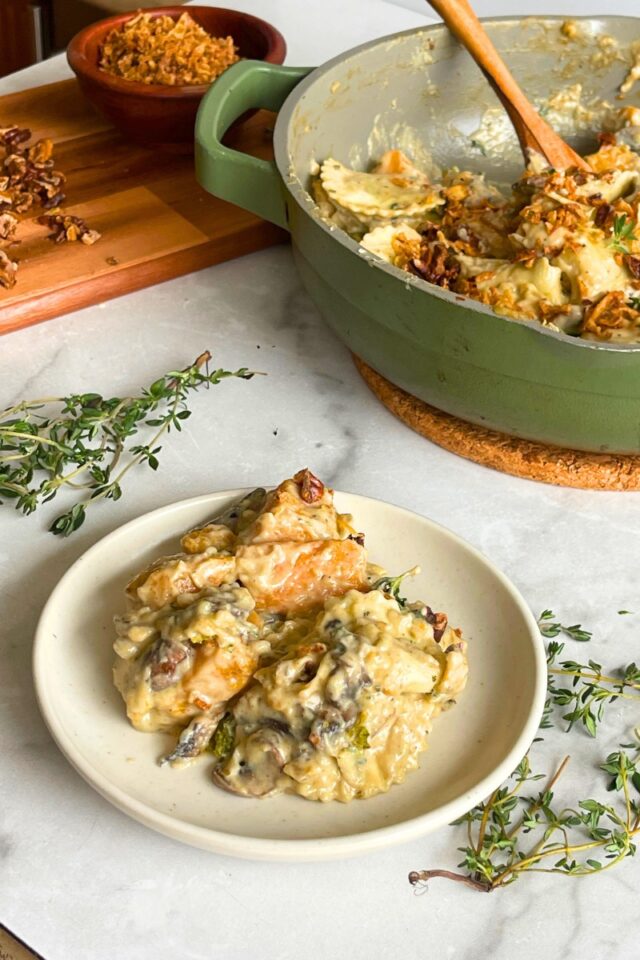 plate of ravioli on a marble countertop with thyme sprigs in front of a green skillet with more ravioli in it