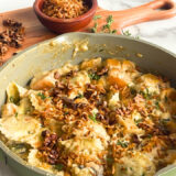 green skillet with butternut squash and ravioli in it in front of a wood cutting board with walnuts on it