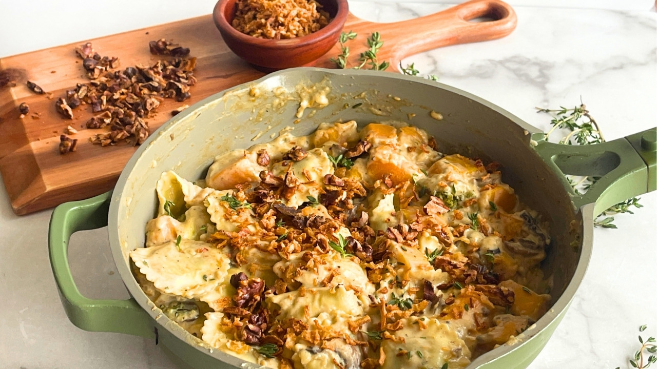 green skillet with butternut squash and ravioli in it in front of a wood cutting board with walnuts on it