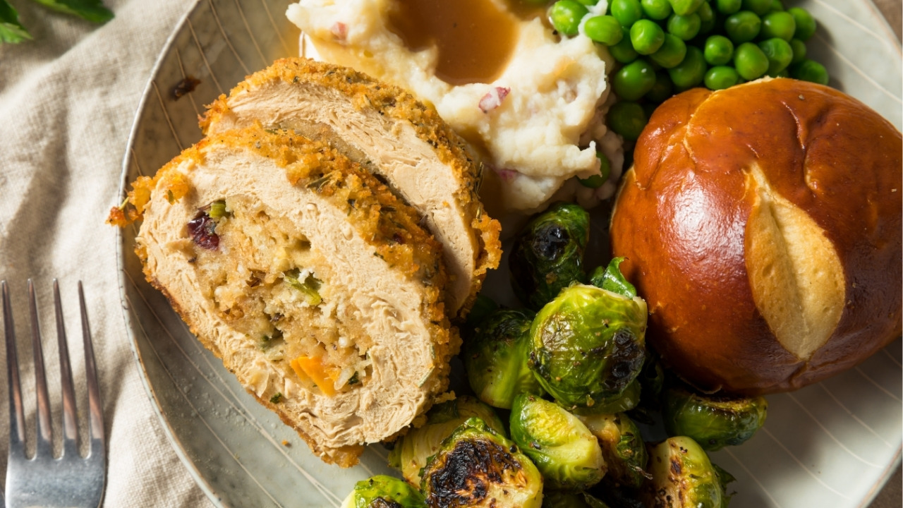 plate full of vegan turkey, Brussels sprouts, mashed potatoes and gravy, and a dinner roll